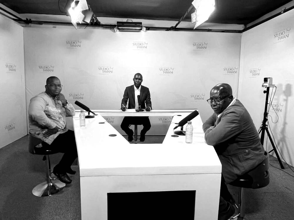 Trois hommes réunis autour d'une table blanche en U, face à des micros, sur le plateau de Studio Tamani pour une émission de débat.