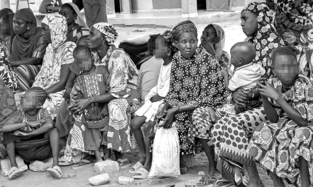 Des femmes et des enfants assis à même le sol attendent devant un bâtiment, des familles parmi celles qui ont trouvé refuge à Macina.