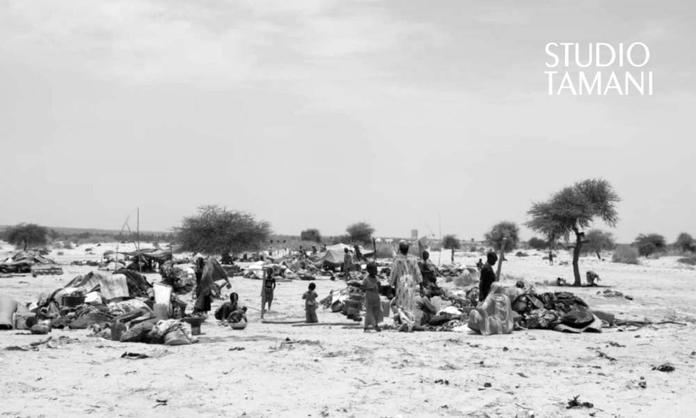 Des habitants, dont des femmes et des enfants, au milieu d'effets personnels et d'abris démontés éparpillés sur le sable d'un campement de la région de Ménaka.