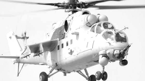 Un hélicoptère d'attaque de type Mi-24, armé de lance-roquettes sous ses ailerons, en vol stationnaire à basse altitude.